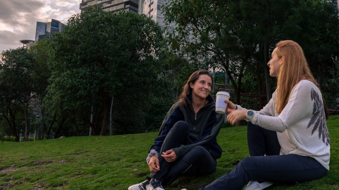 Two women enjoying coffee and conversation in a vibrant park setting in Mexico City.