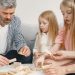 Four family members of different ages engage with toy blocks on a table indoors.