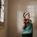 Senior woman in a brightly lit room exercises with dumbbells, promoting fitness at home.